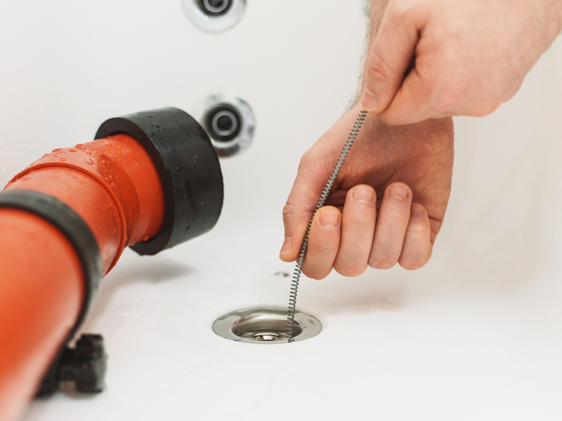 man using drain snake to unclog a drain